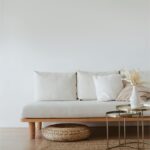 Canapea minimalistă cu cadru din lemn, perne albe și decorațiuni discrete într-un decor de design interior scandinav.