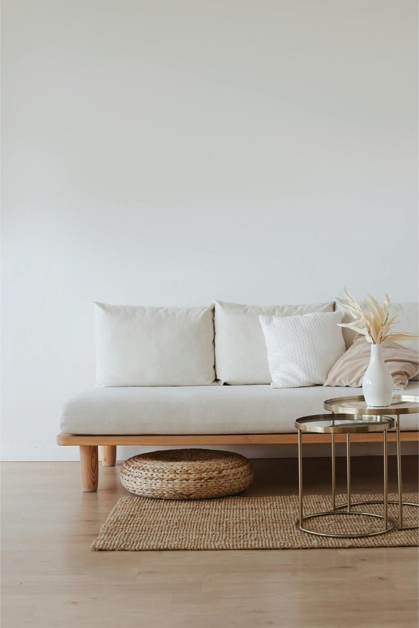 Canapea minimalistă cu cadru din lemn, perne albe și decorațiuni discrete într-un decor de design interior scandinav.